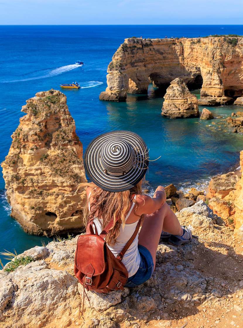Mujer admirando la vista panorámica de la costa del Algarve, con aguas cristalinas y un acantilado rodeado de vegetación