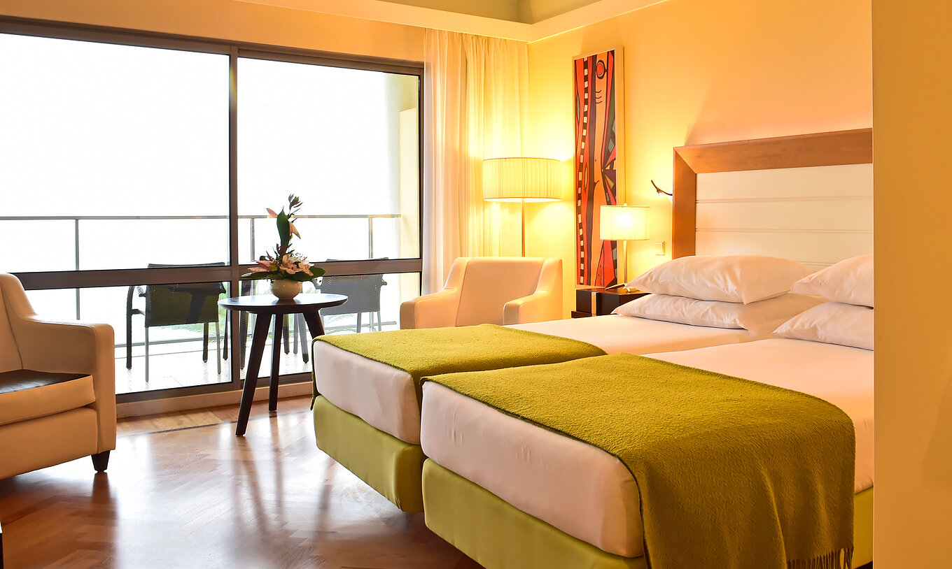 El Superior del Pestana Promenade tiene dos camas con un edredón verde y una ventana grande al balcón