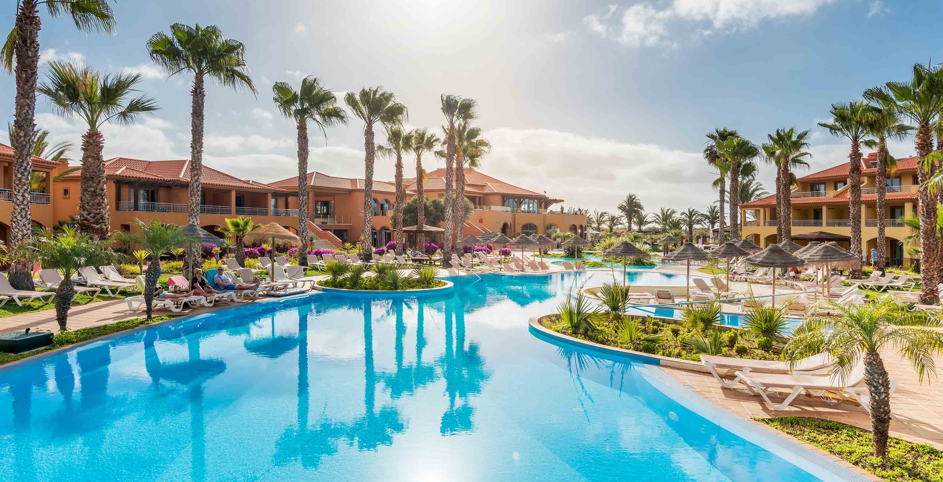 Amplia piscina azul Pestana Porto Santo, tumbonas, palmeras, edificios bajo cielo soleado