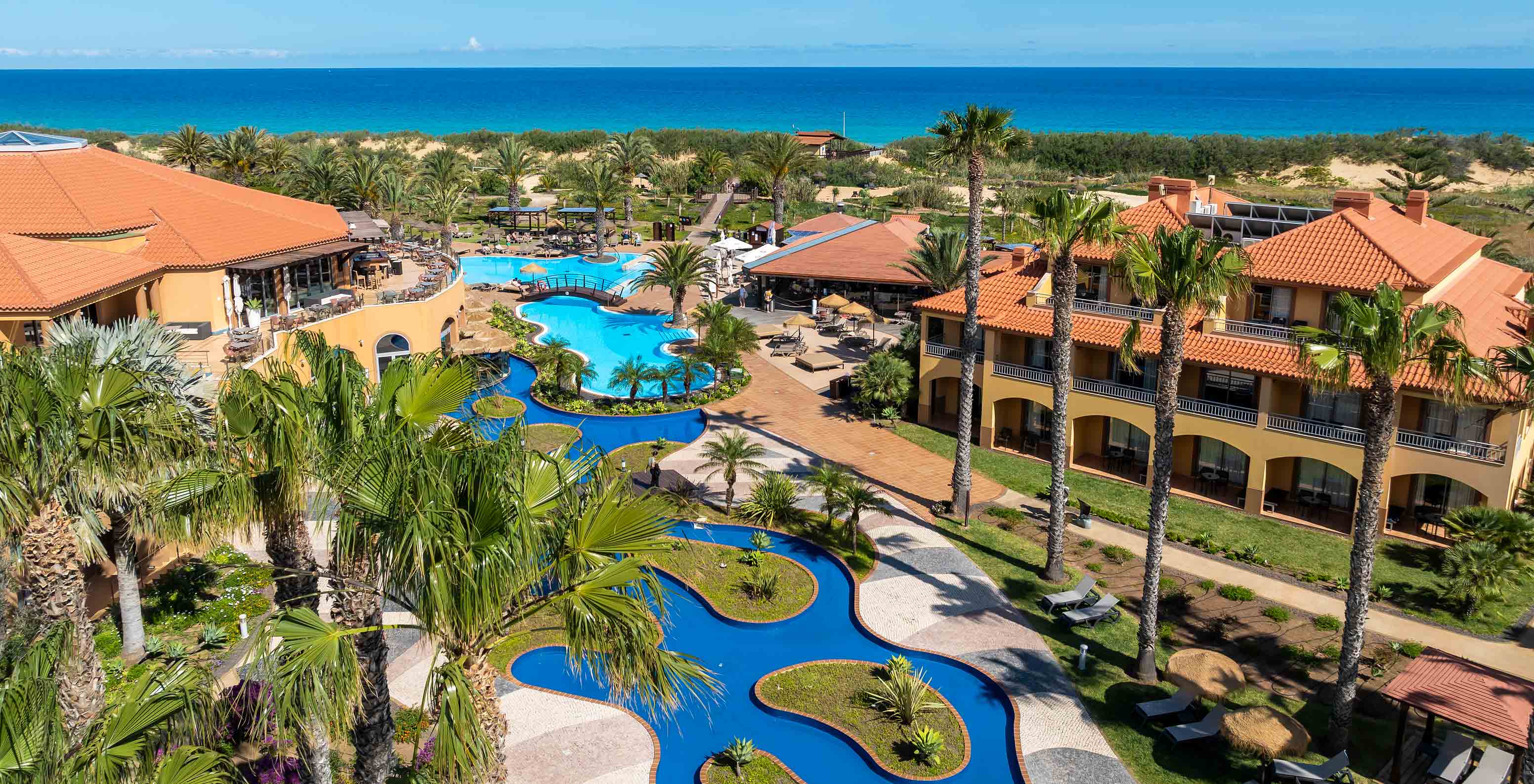 Piscina exterior azul del Pestana Porto Santo All Inclusive, rodeada de palmeras, villas y jardines