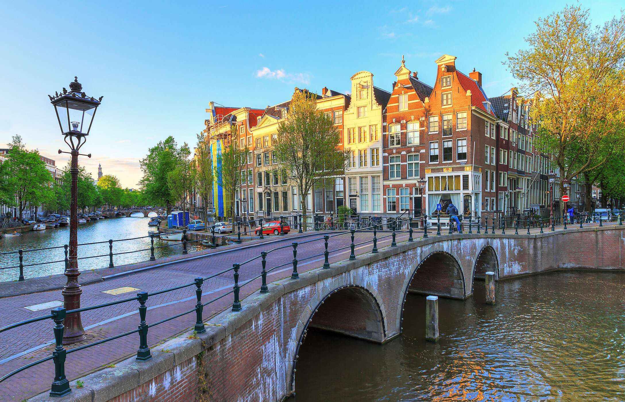 Vista de un puente de ladrillo rojo sobre el canal Keizersgracht, con edificios típicos y árboles al fondo