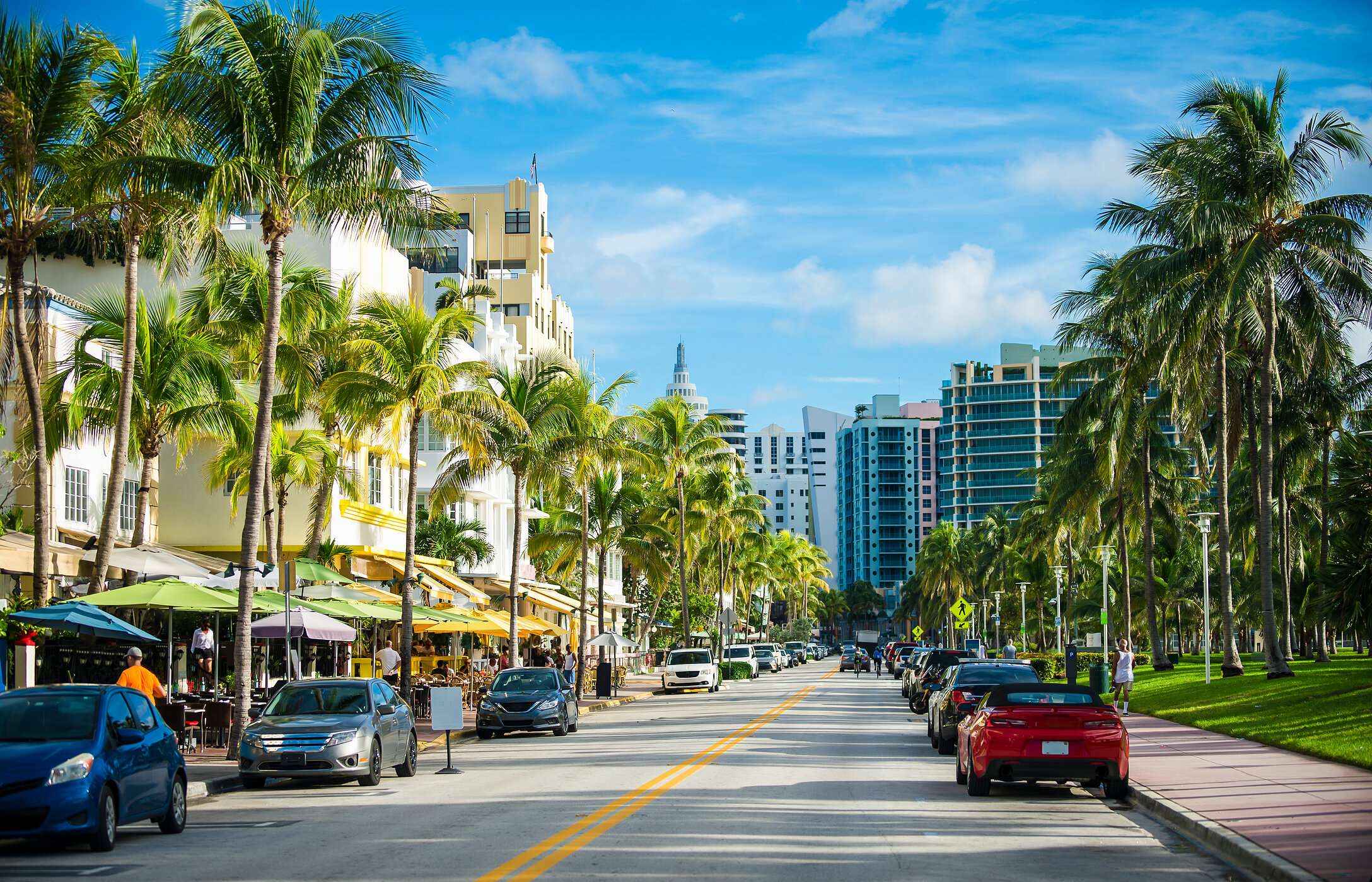 Vista sobre Ocean Drive en Miami, con altas palmeras, edificios Art Decó y varios coches estacionados