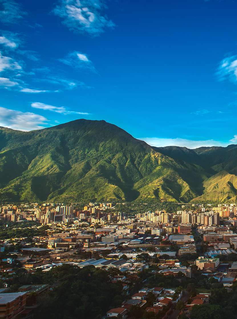 Vista aérea de la ciudad de Caracas, con edificios altos, contrastando con la naturaleza montañosa y el cielo azul