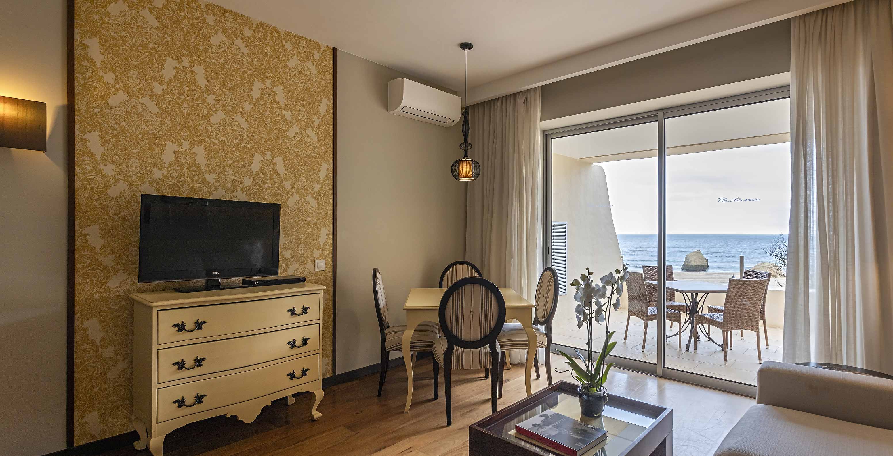 De Cliff Suite T1 in Pestana Alvor Praia heeft een woonkamer met tv en een balkon met tafel, stoelen en zeezicht