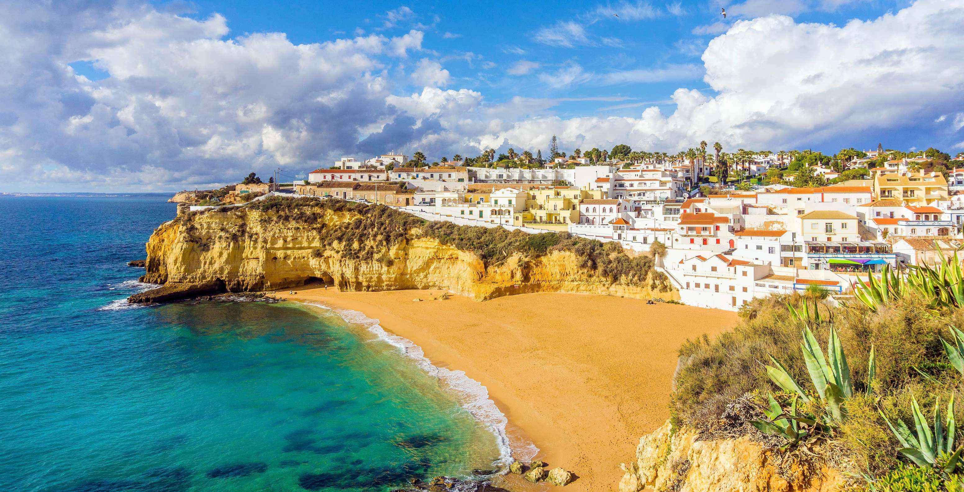 Strand van Carvoeiro met blauw water, de typische kliffen van de Algarve en het dorp Carvoeiro op de achtergrond