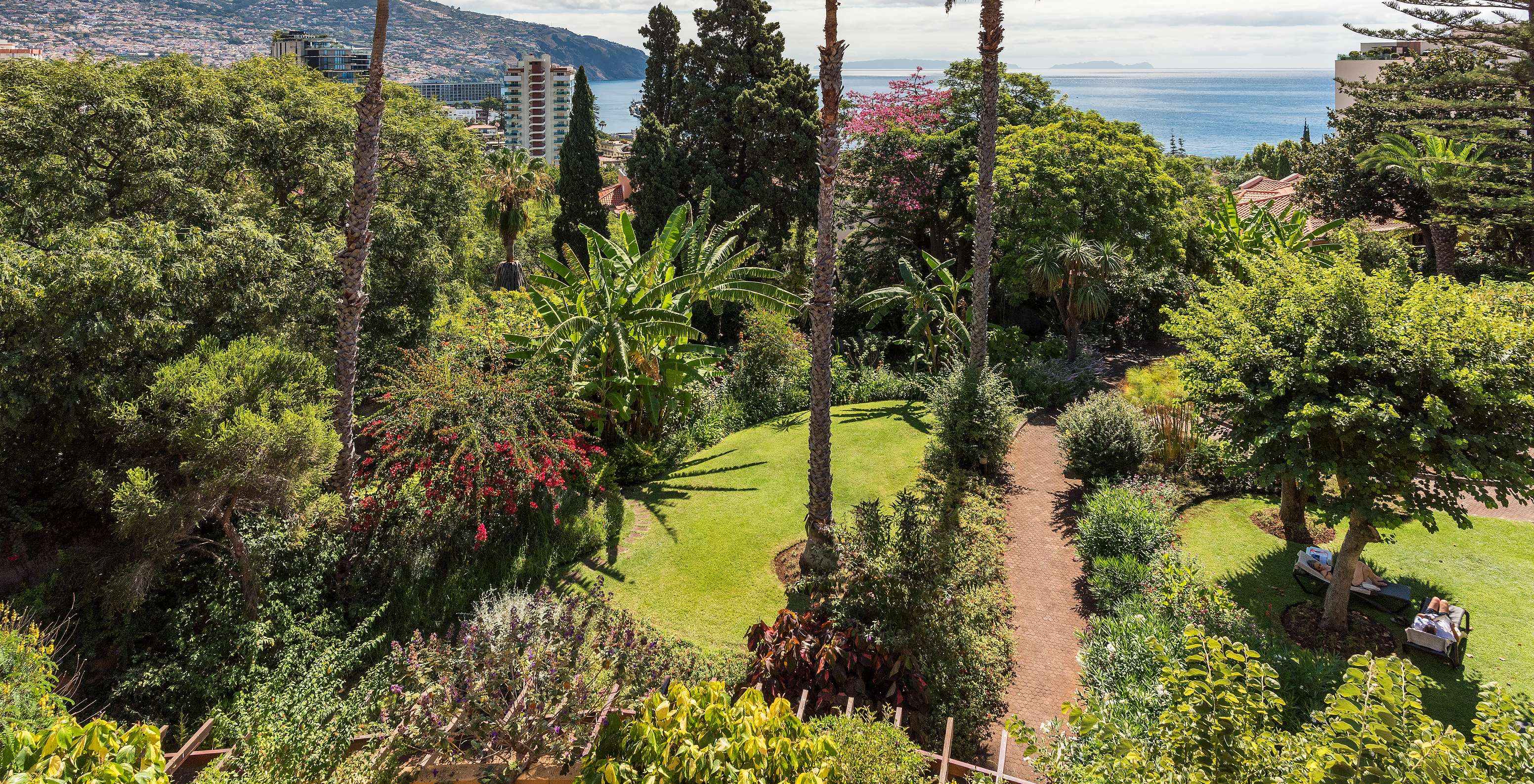Luchtfoto van groene tuinen met bloemen en palmbomen, van Pestana Village, een Romantisch Hotel in Funchal, Madeira