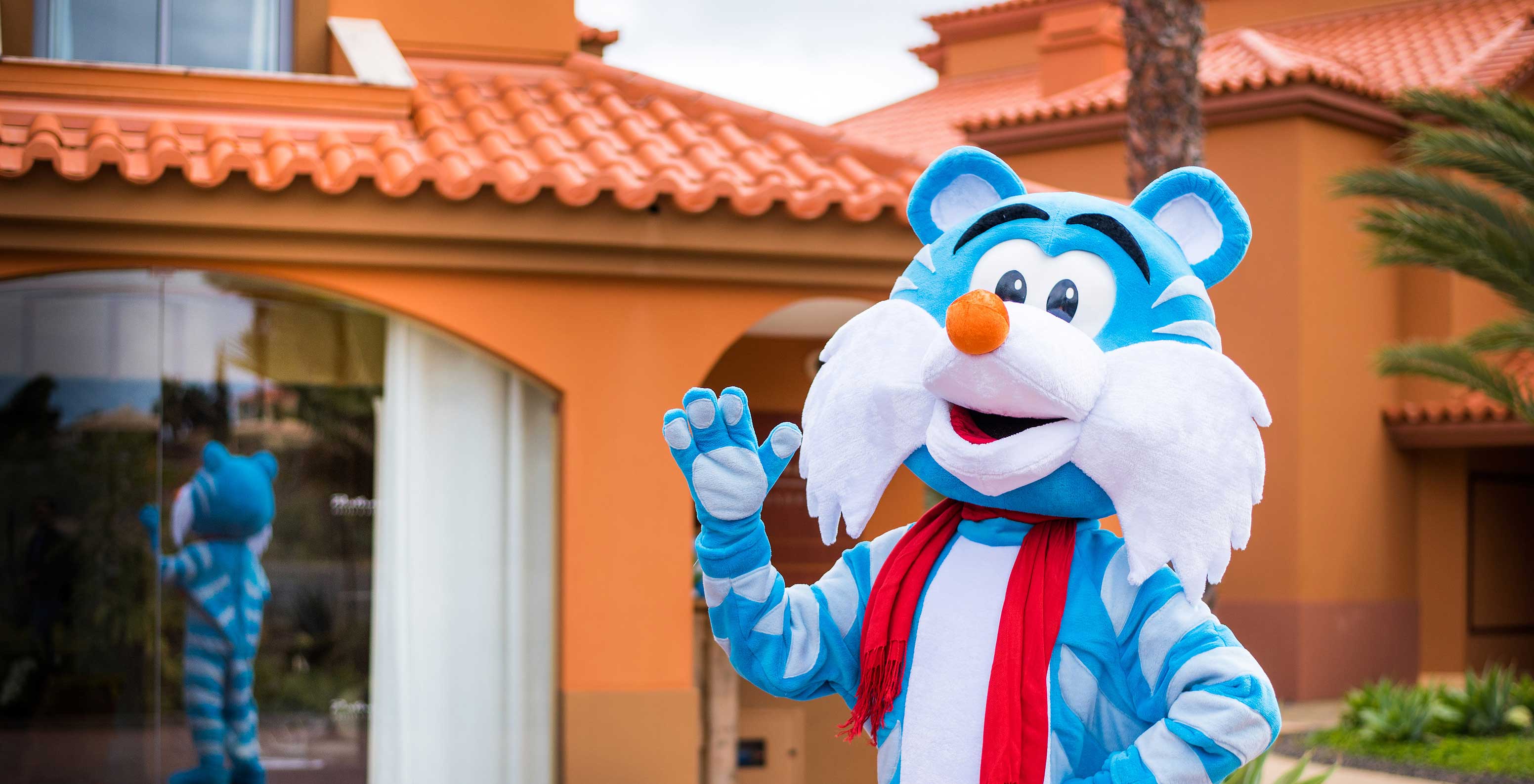 Blauw-witte tijgermascotte zwaait voor Pestana Porto Santo, reflectie zichtbaar raam