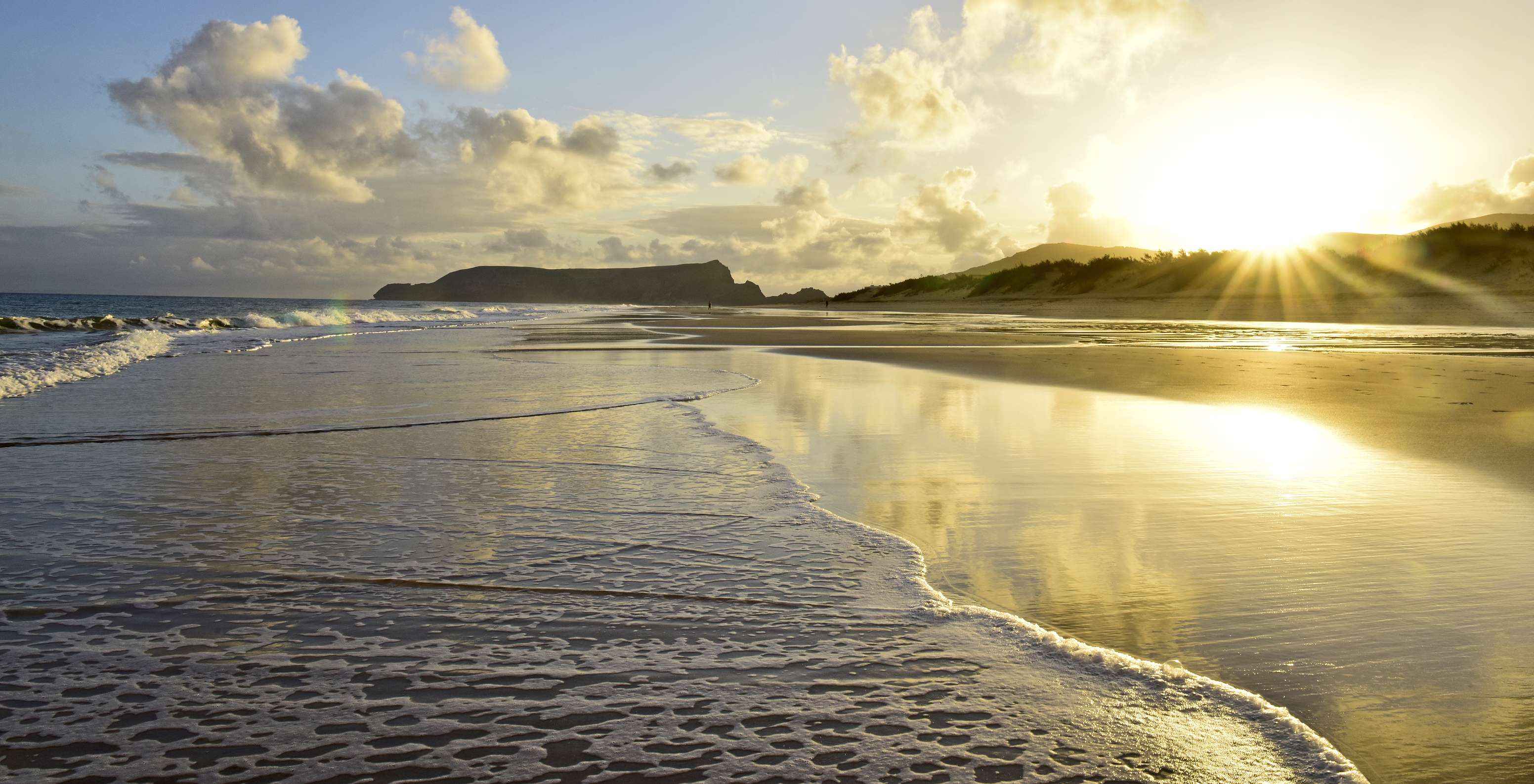 Zonsondergang op het strand van Porto Santo, met een lucht vol oranje wolken en de zon die gouden stralen op de zee werpt