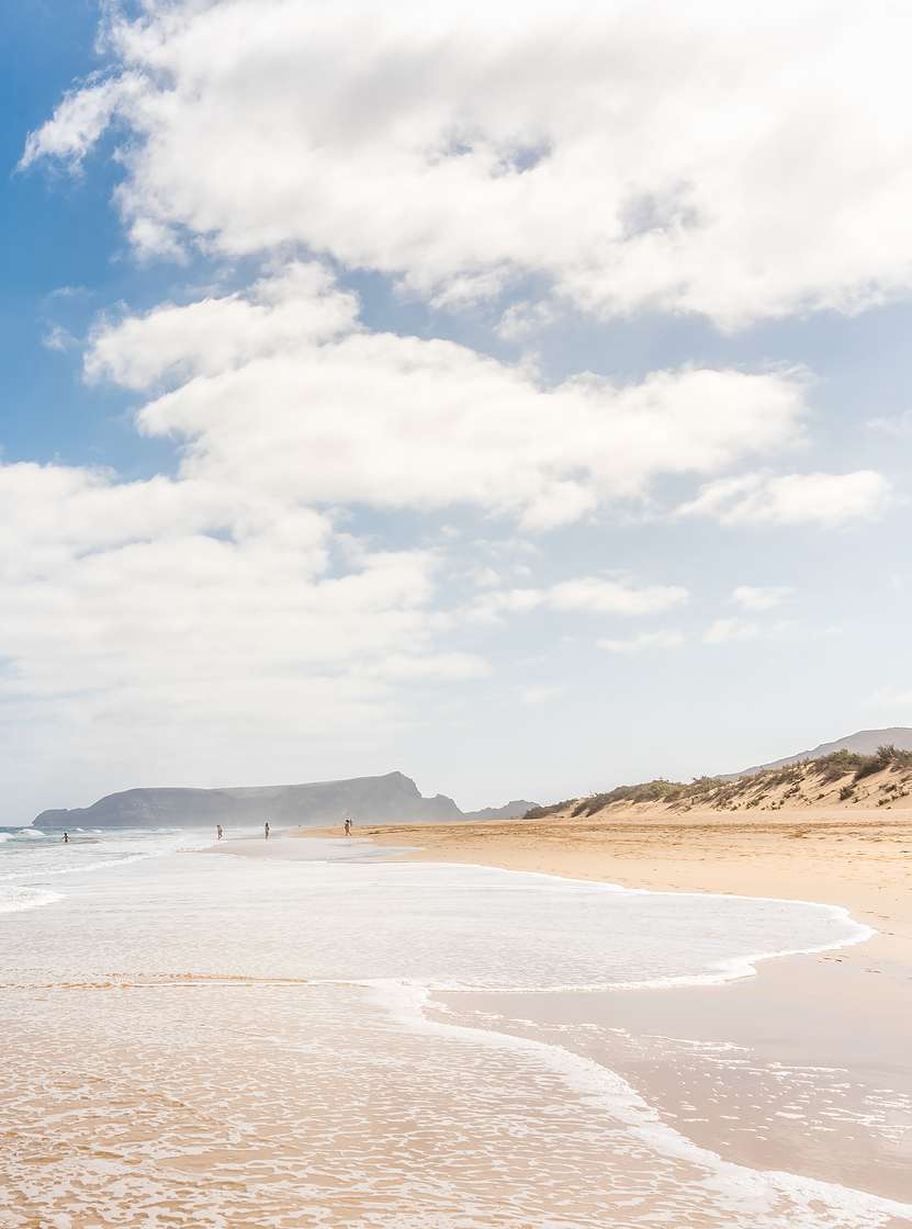 Lang strand in Porto Santo met licht zand, rustige golven en een blauwe lucht met enkele wolken