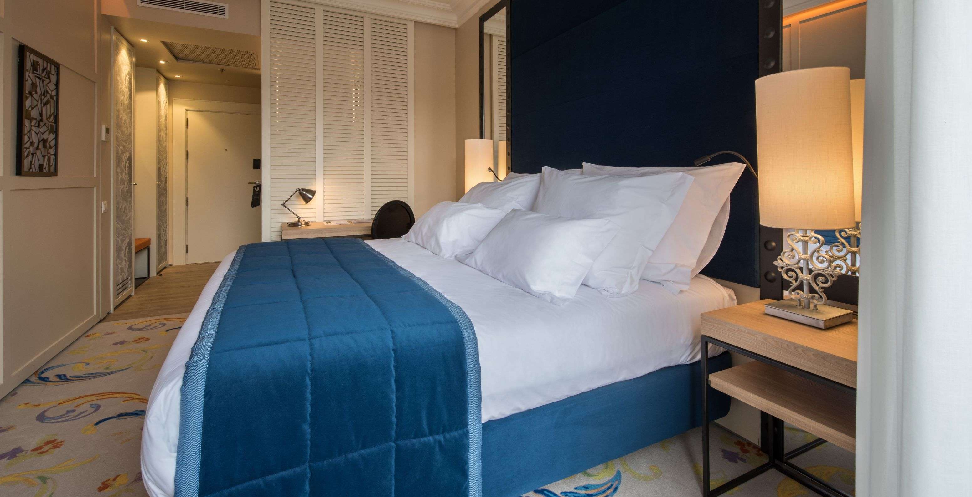 De Superior Plus Kamer in Pestana Collection Plaza Mayor heeft een tweepersoonsbed met een blauwe sprei en een tapijt.