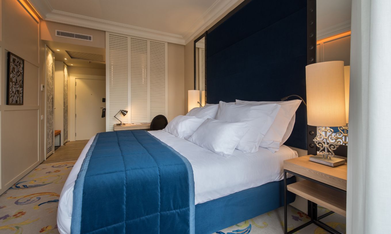 De Superior Plus Kamer in Pestana Plaza Mayor Madrid heeft een tweepersoonsbed met een blauwe sprei en een tapijt.