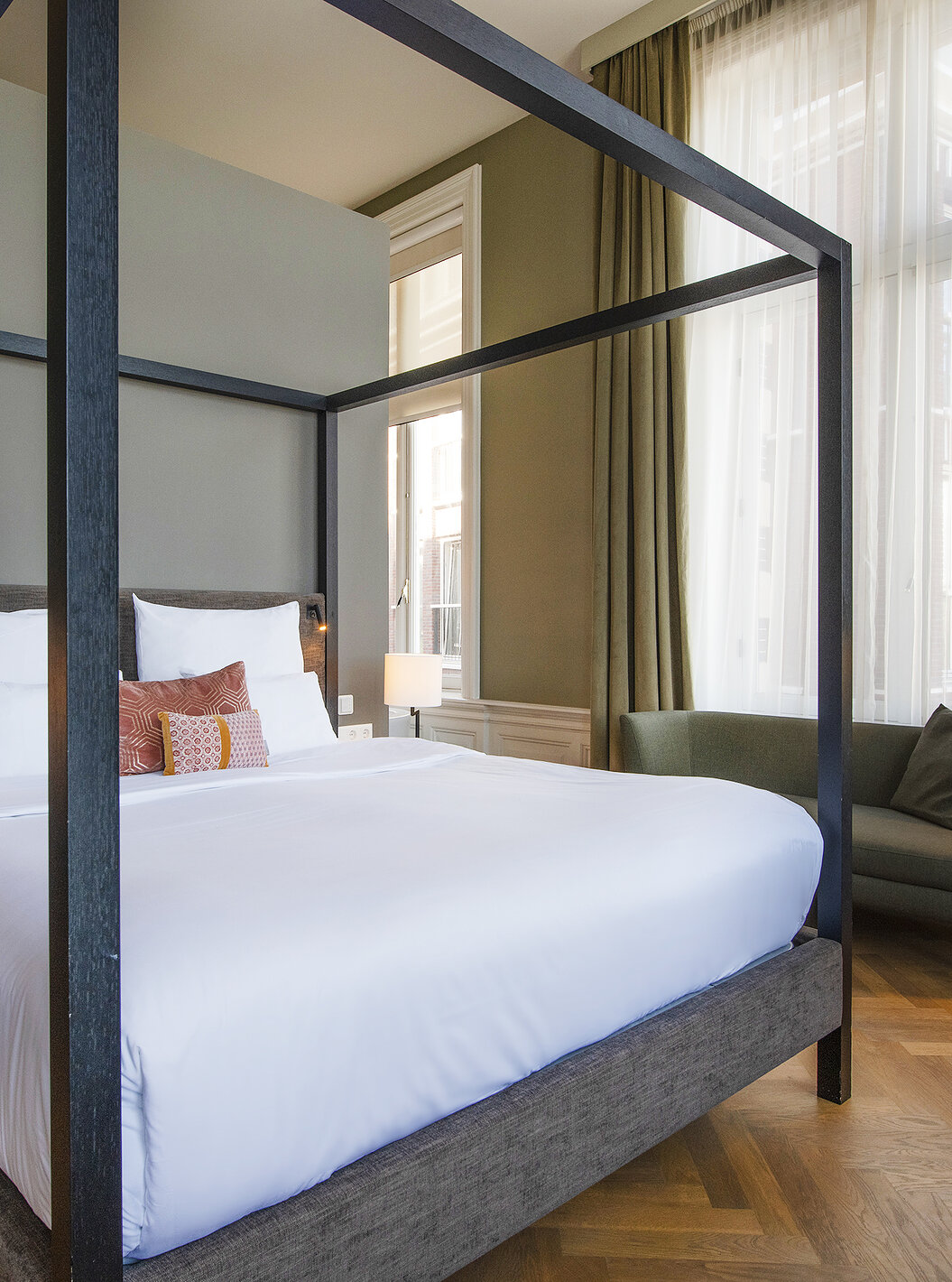 Junior Suite - River View van Pestana Amsterdam Riverside heeft tweepersoonsbed met hemelbed en groene bank