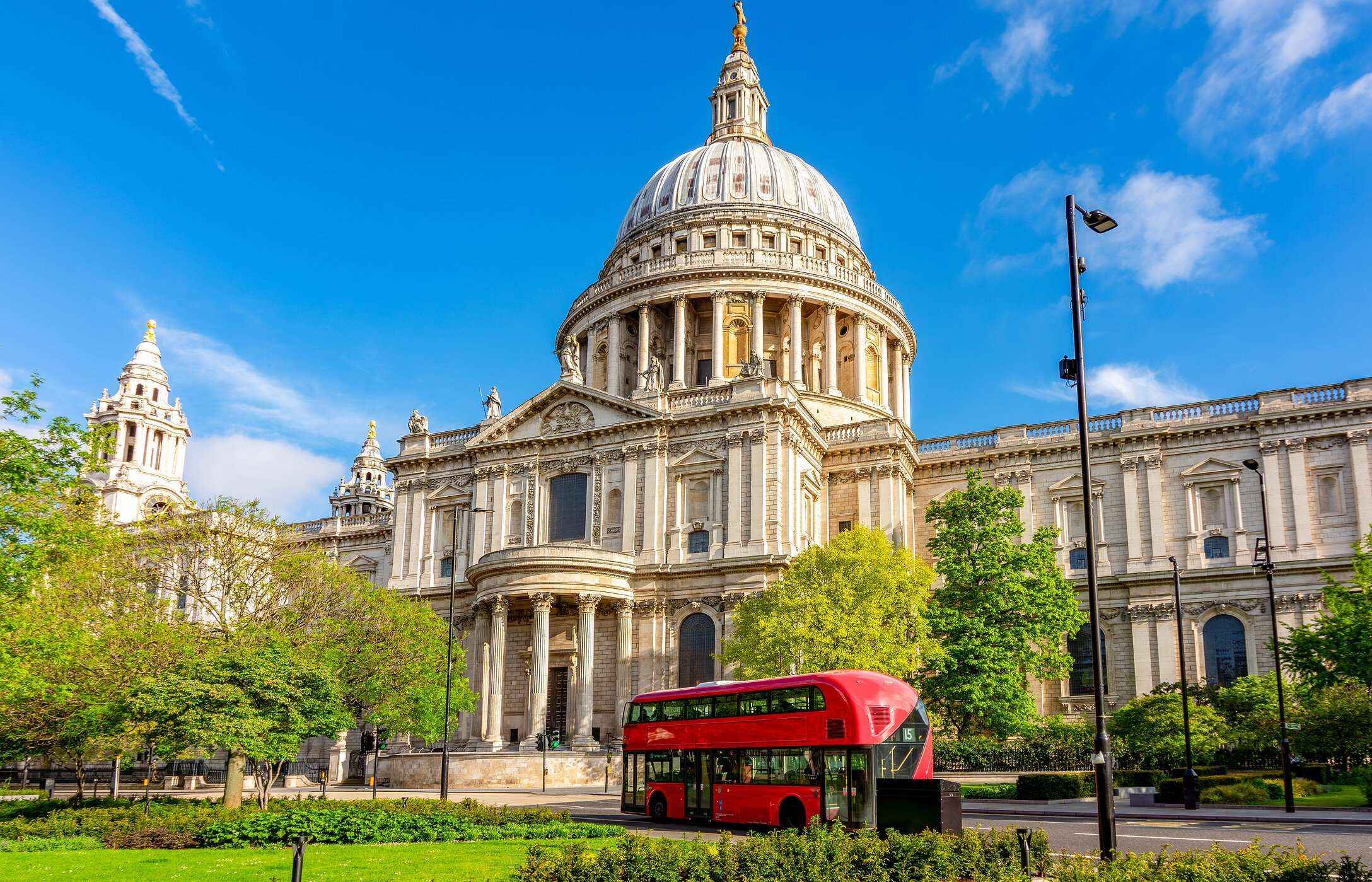 Stedelijk uitzicht op de St Paul's kathedraal in Londen, met een rode bus ervoor en een tuin