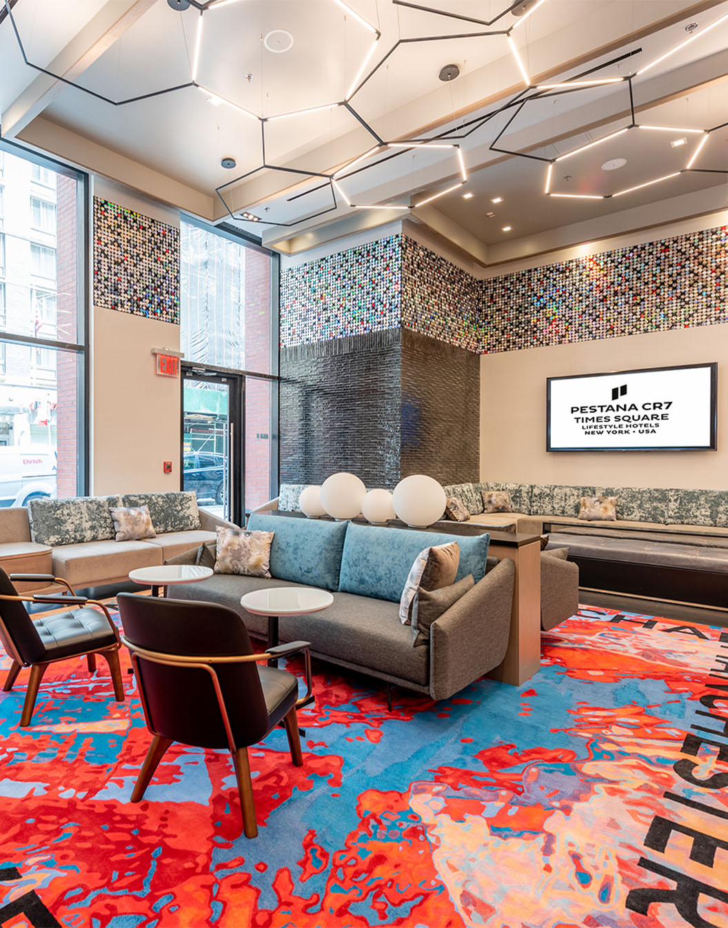 Lobby Pestana CR7 Times Square met comfortabele banken, stoelen en kleurrijk tapijt