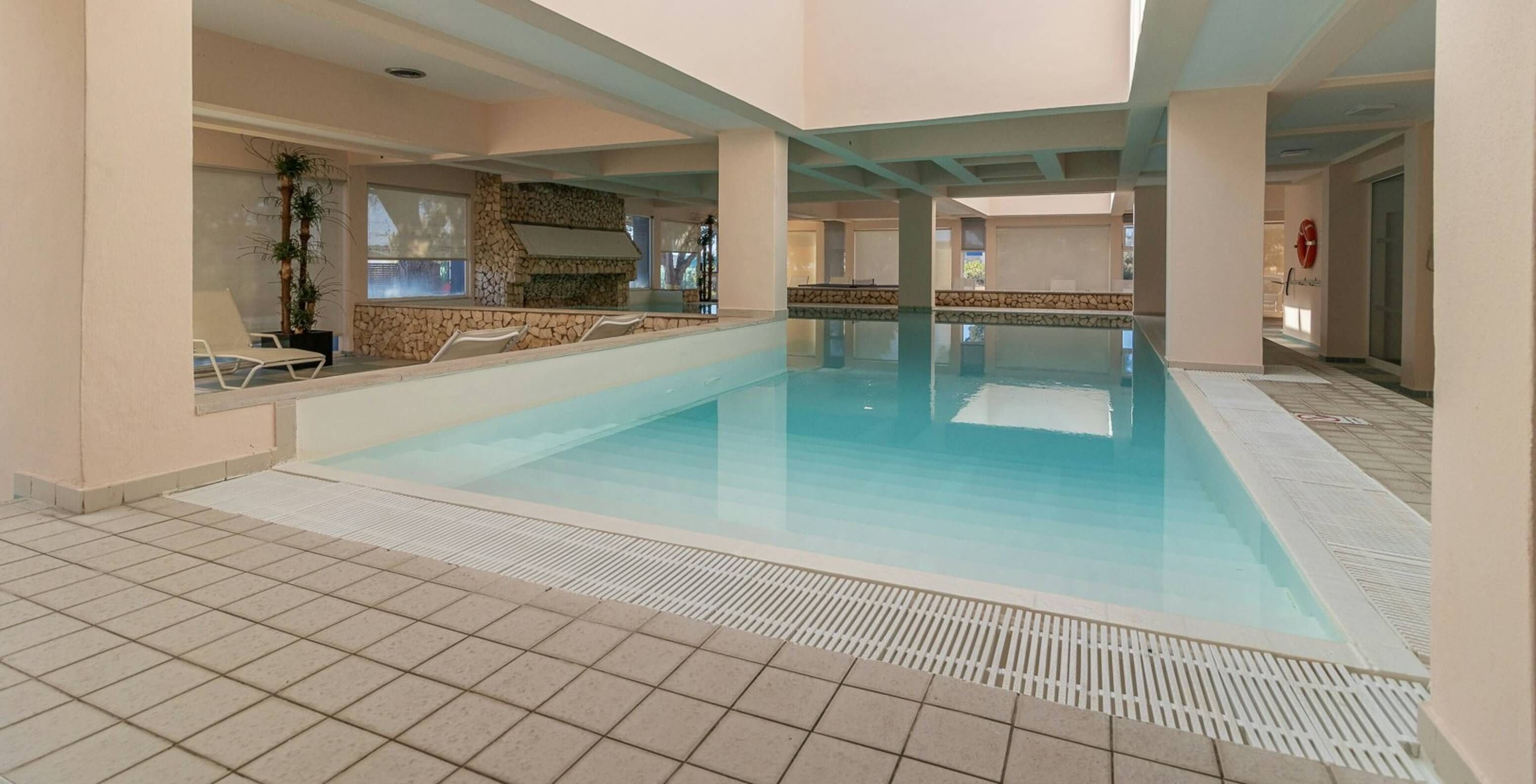 Piscina interior com luz natural e espreguiçadeiras no aparthotel em frente ao mar