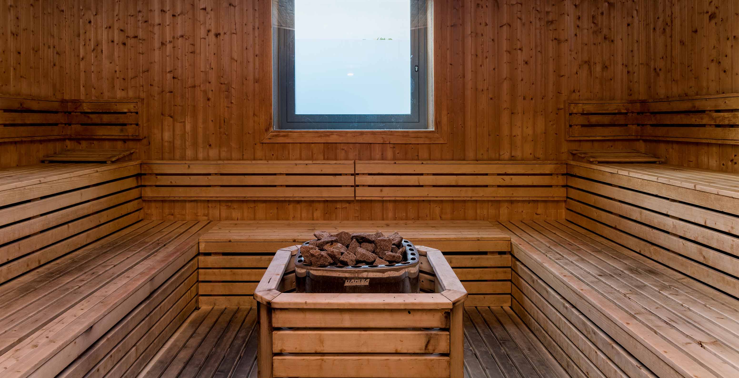 Interior de uma sauna de madeira clara no Pestana Porto Santo, com pedras quentes no centro e uma pequena janela