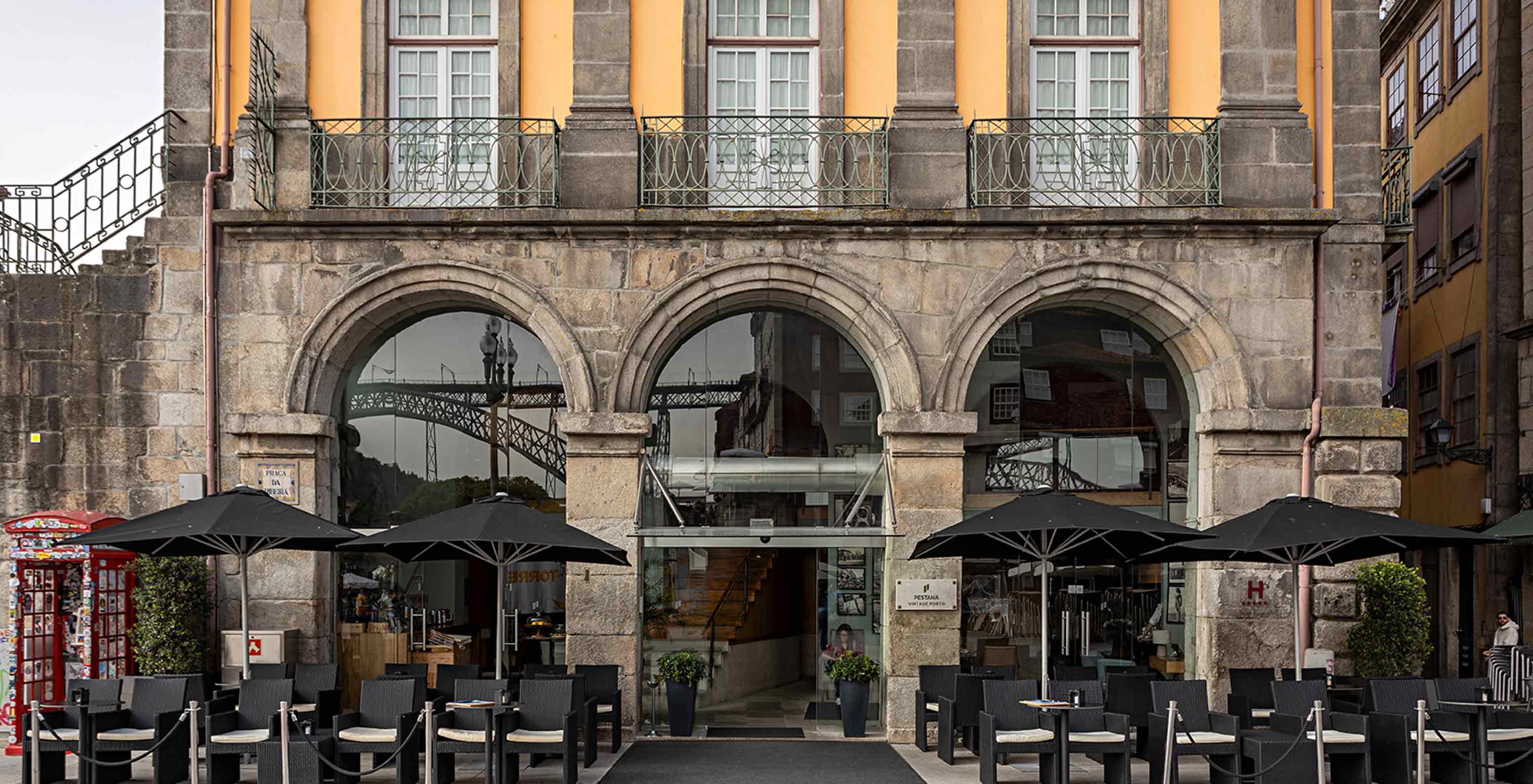 Fachada exterior do Pestana Vintage Porto com acesso a um pátio que tem mesas com cadeiras e chapéus de sol