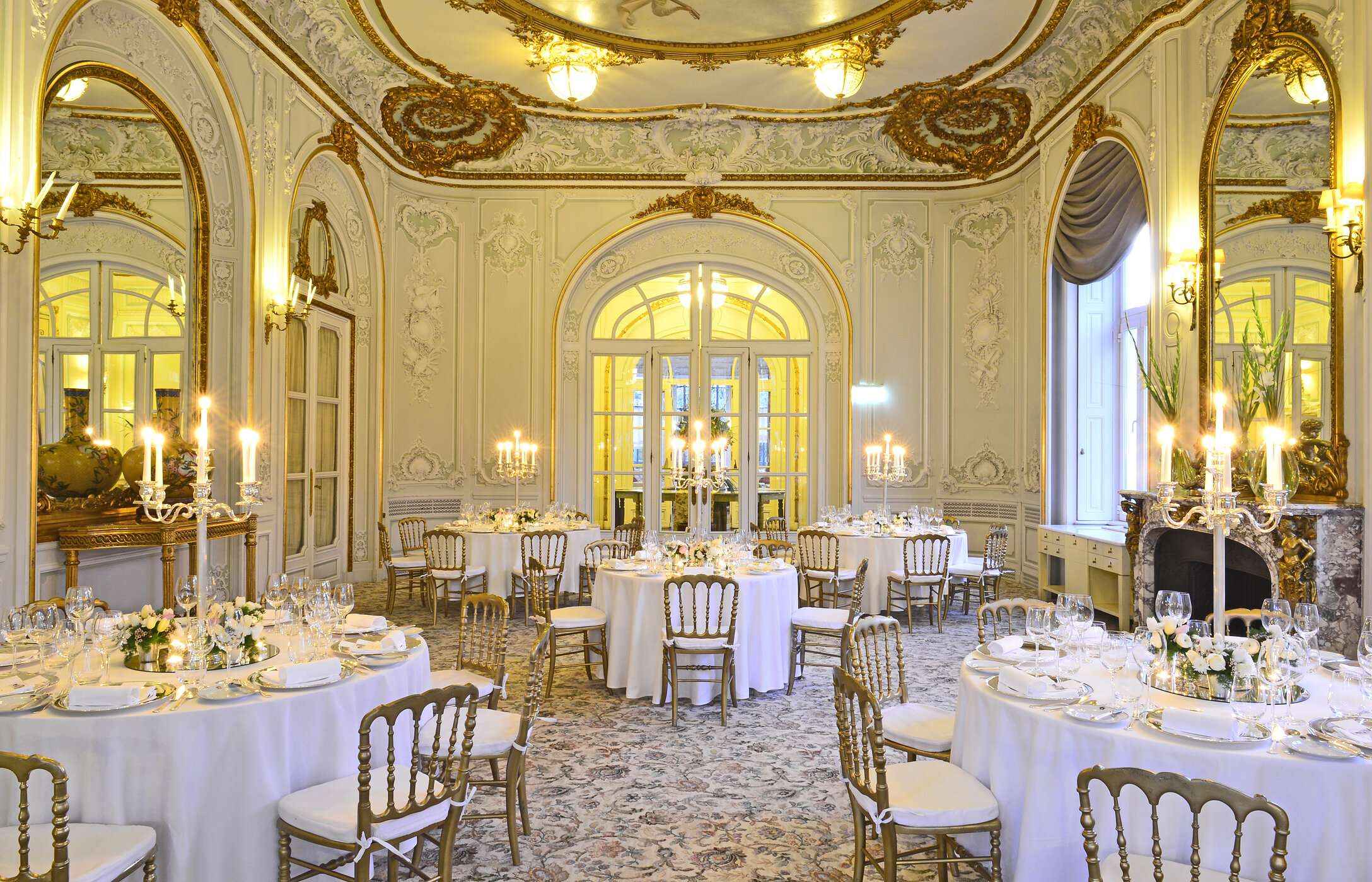 Casamento em sala elegante, com tapete estampado, paredes adornadas com detalhe de ouro e mesas com arranjos florais