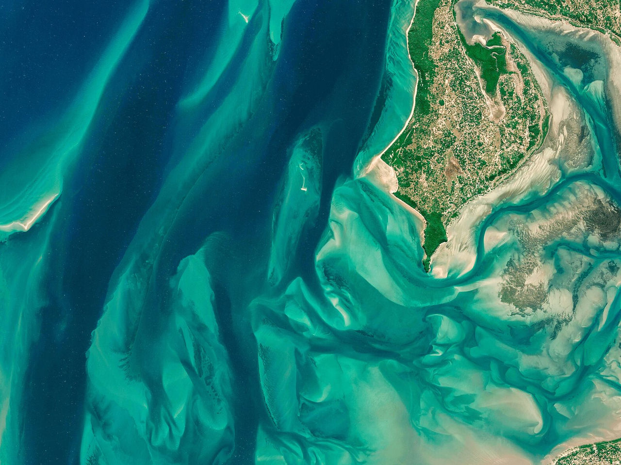 Luchtzicht over groene vlaktes en de oceaan, waarbij een asymmetrisch patroon van zand en water ontstaat