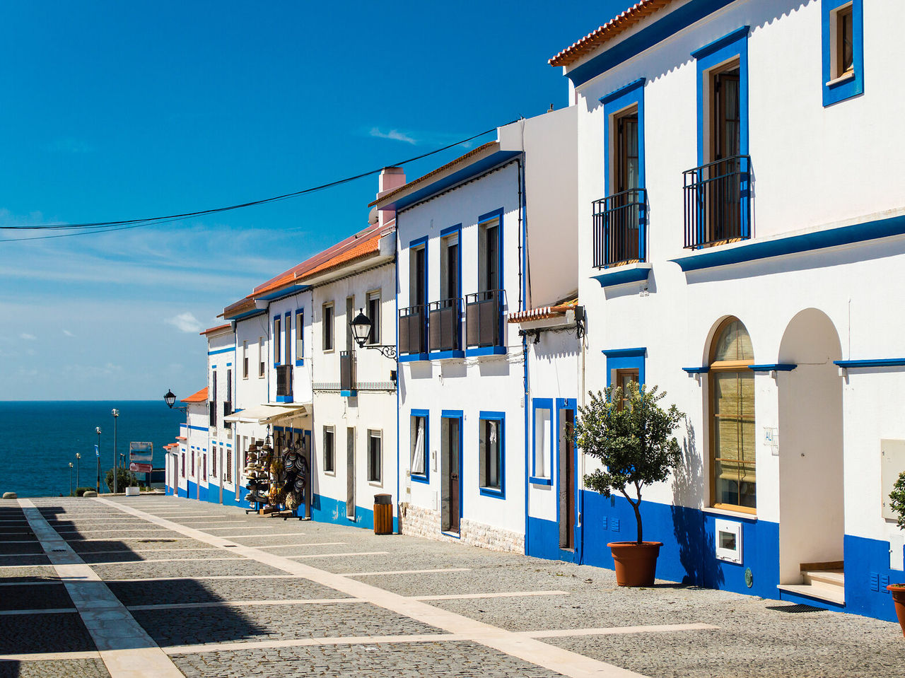 Straat met typische huizen uit de Alentejo-regio, wit en blauw met potten bij de deur en een geweldig uitzicht op de oceaan