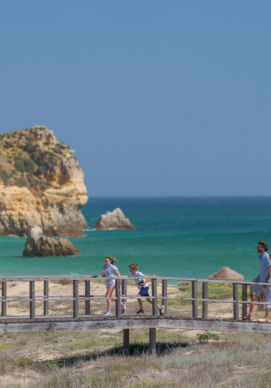 Houten loopbruggen van Praia do Alvor, met de zee op de achtergrond en twee kinderen die rennen met hun ouders achter hen