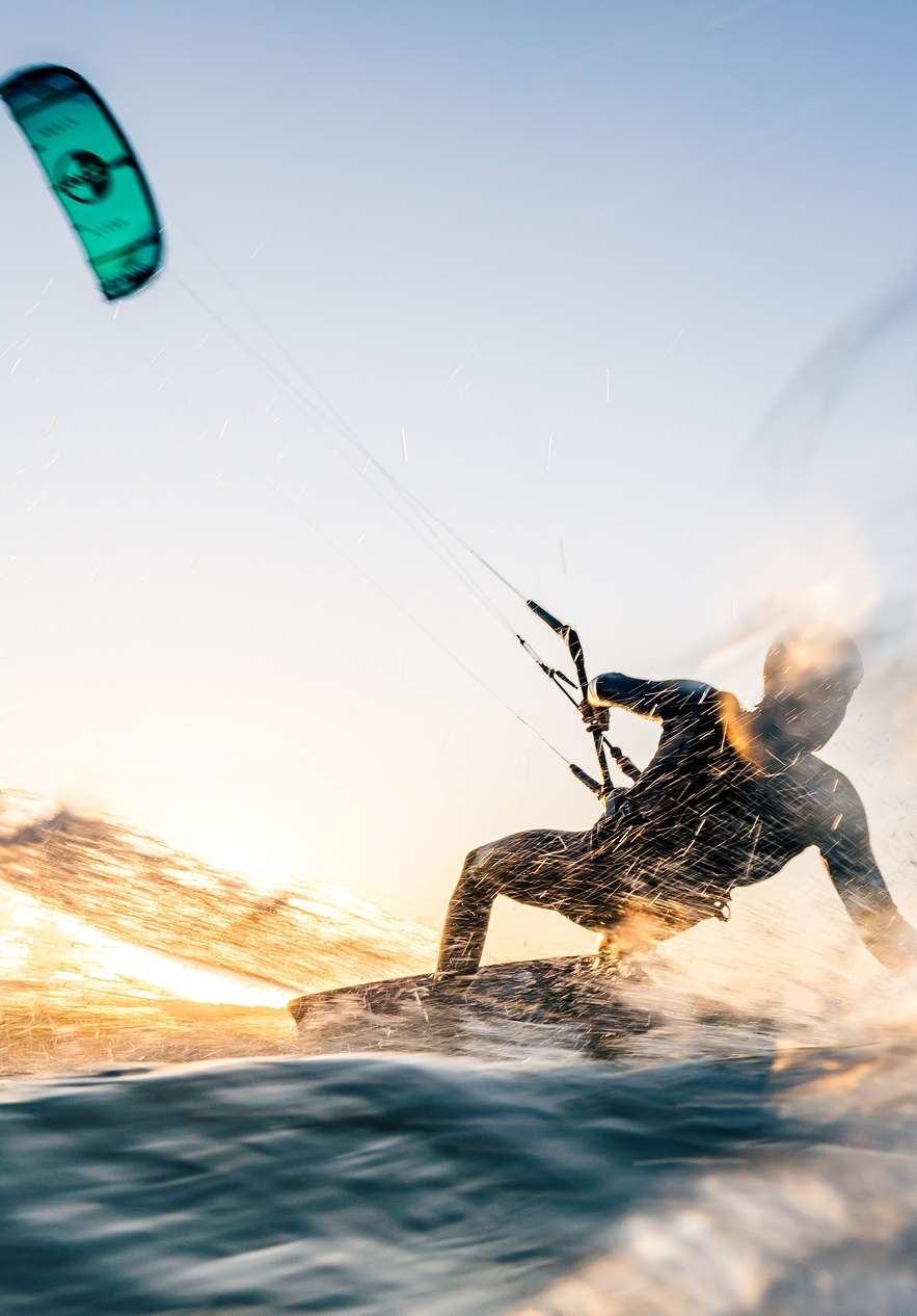 Iemand doet kitesurfen op een zonnig strand, met een blauwe lucht en helder water