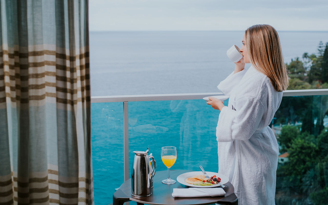 Vrouw ontbijt op het balkon in een badjas, genietend van het uitzicht op de oceaan, in een hotel aan zee