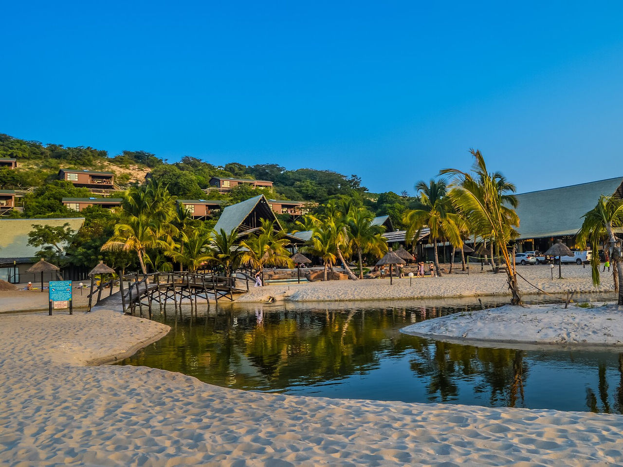 Beach in Maputo with a river passing through the sand, a bridge to cross the small river and scattered palm trees
