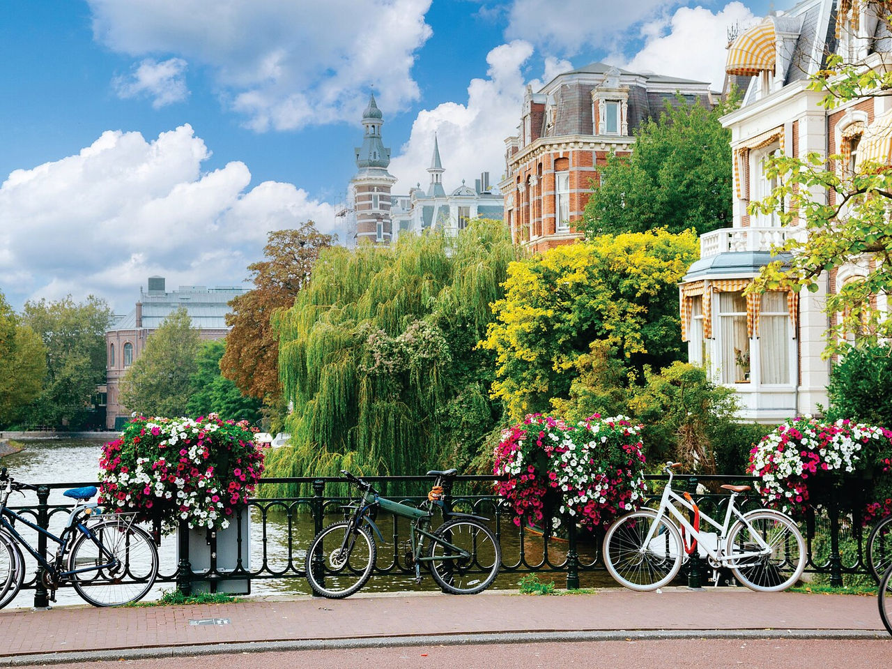 Bridge over a canal in Amsterdam, with parked bicycles, colorful flowers, and typical buildings in the background
