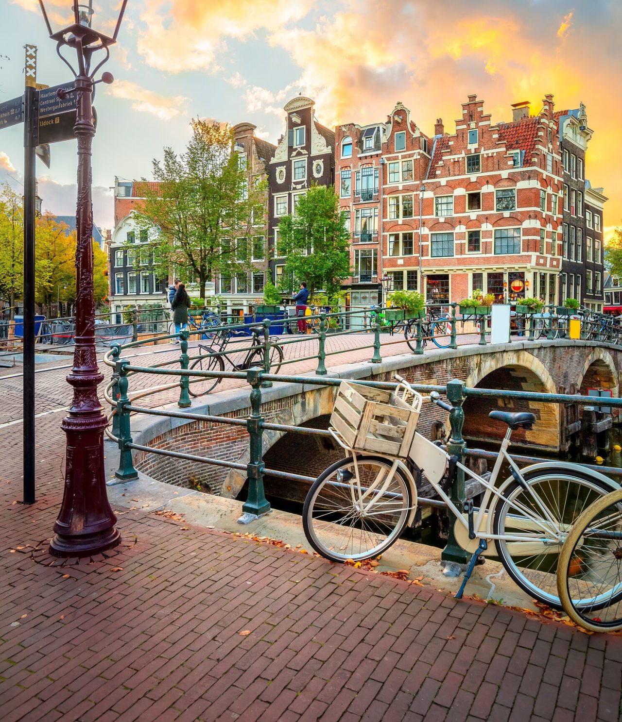 Pedestrian bridge in Amsterdam over a canal, with typical bicycles, people walking, and buildings in the background