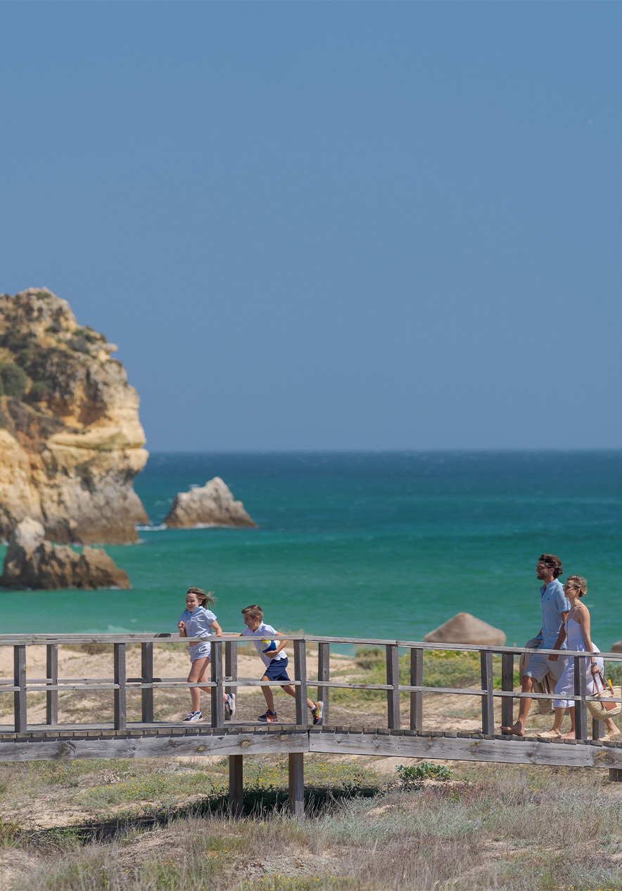 Wooden walkway of Alvor beaches with the sea in the background and two children running with their parents behind