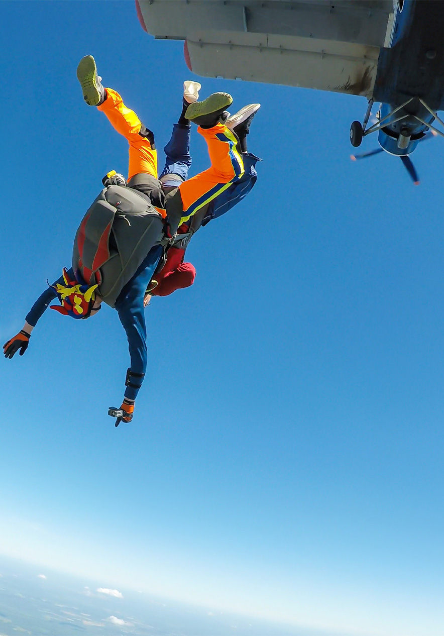 Two people jumping out of a plane with parachutes and colorful suits against a clear sky with the plane flying above
