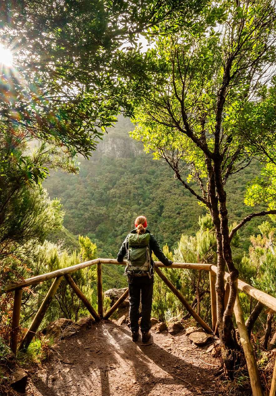 Woman peeking through a clearing in nature next to a wooden fence while carrying a backpack