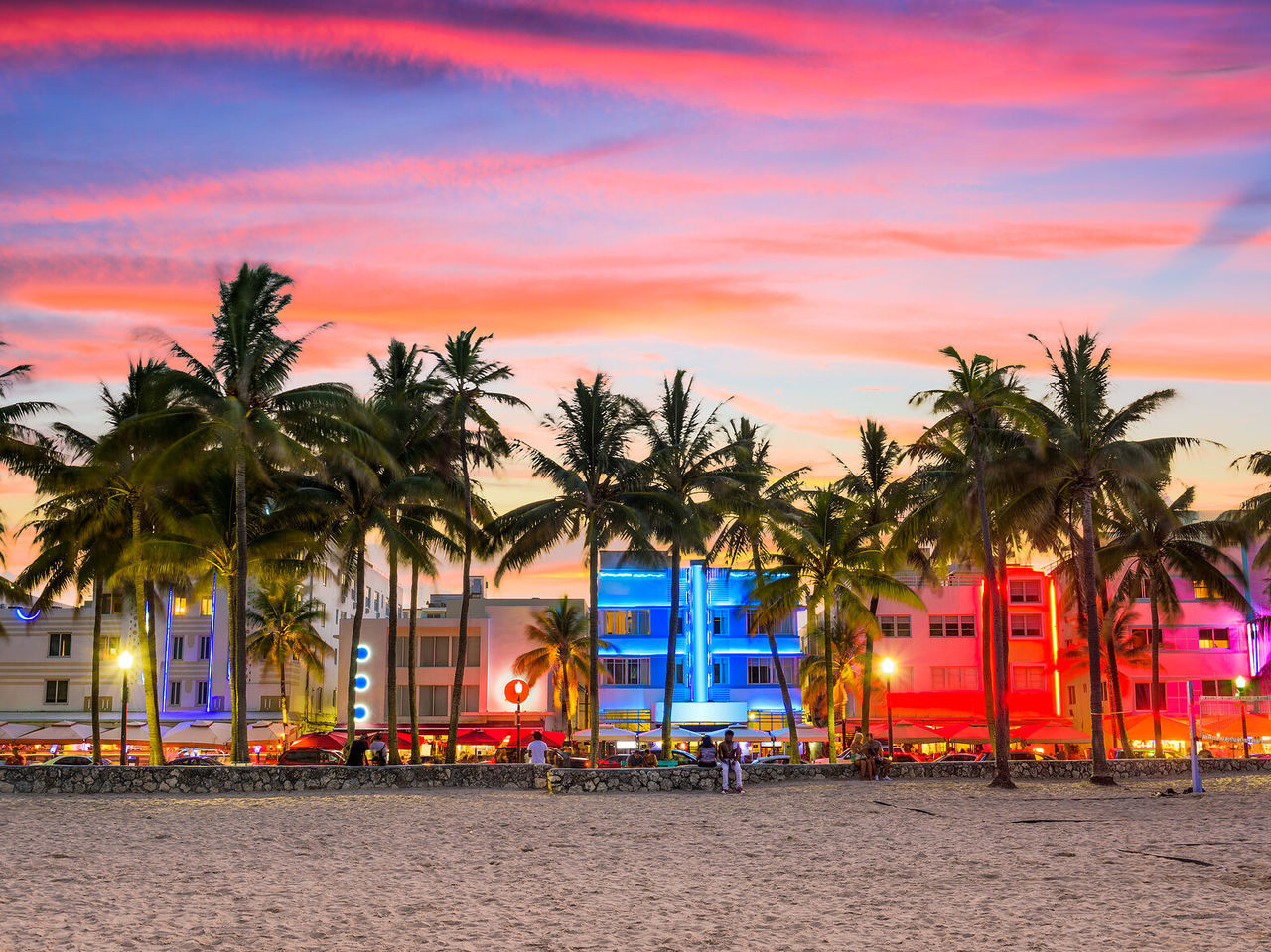 Vibrant sunset at Miami Beach, with silhouetted palm trees and illuminated Art Deco buildings