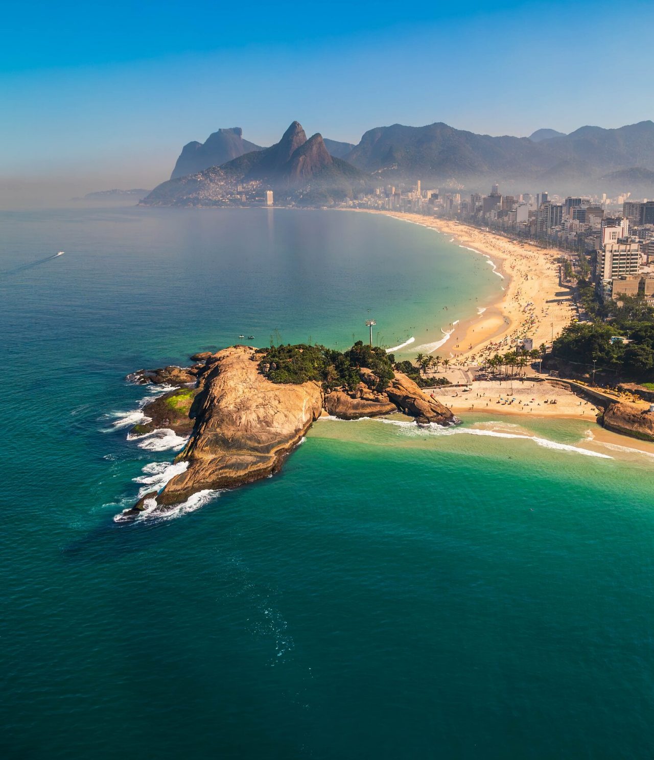 Aerial view of Rio de Janeiro, with mountains in the background, white sandy beach, and turquoise blue sea